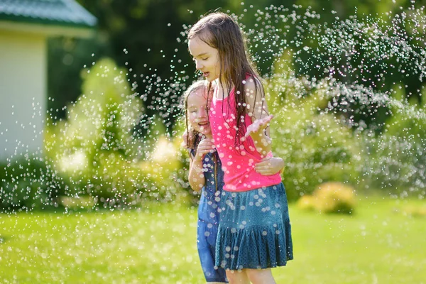 日当たりの良い夏の日に裏庭にスプリンクラーで遊ぶ愛らしい女の子 かわいい子供たちは 水を屋外に楽しんで 面白い夏ゲーム子供のため — ストック写真