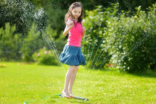在阳光明媚的夏日 一个可爱的小女孩在后院里玩洒水车 可爱的孩子在户外享受水的乐趣 有趣的夏季游戏为孩子们 — 图库照片