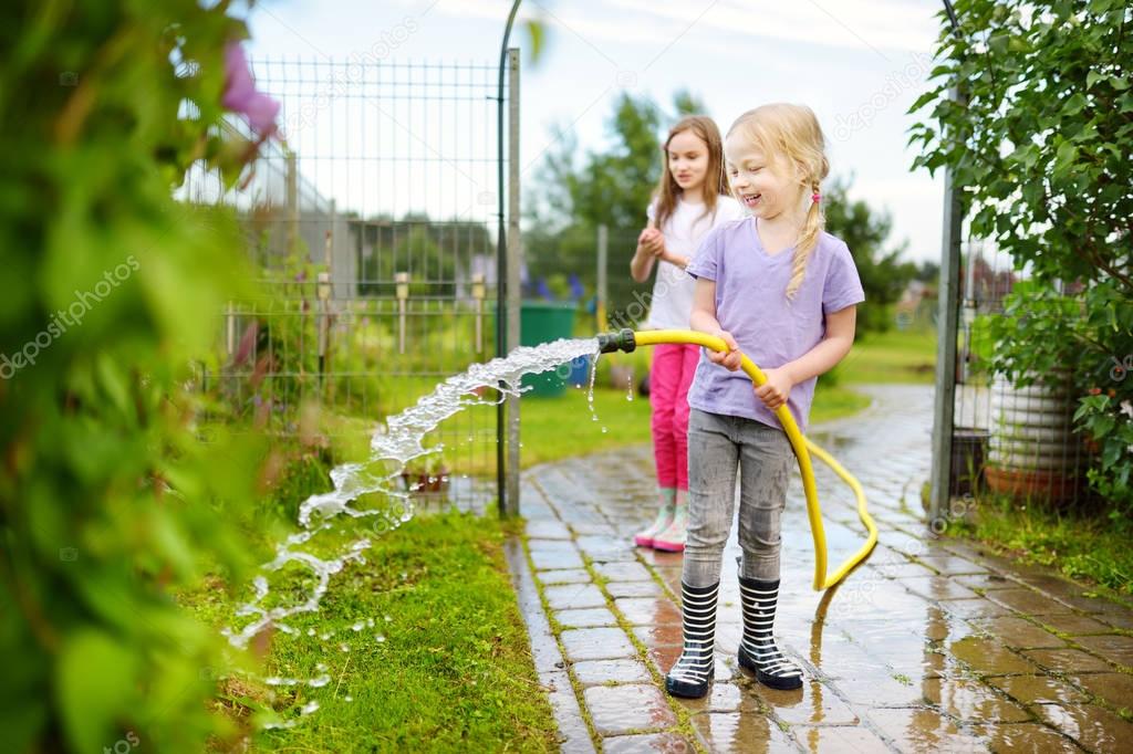 Adorable little girls playing with a garden hose on warm summer day. Outdoor activities for kids.