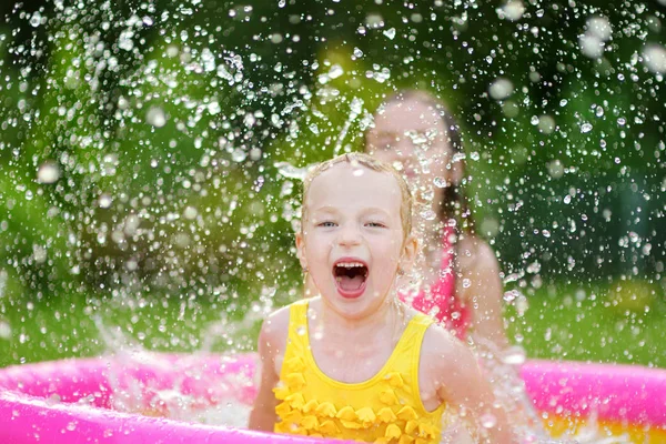 Adorable little girls playing in inflatable baby pool. Happy kids splashing in colorful garden play center on hot summer day. Summer activities for kids.