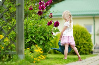 Cute little girl watering flowers in the garden at summer day. Child using garden hose on sunny day. Mommys little helper. clipart