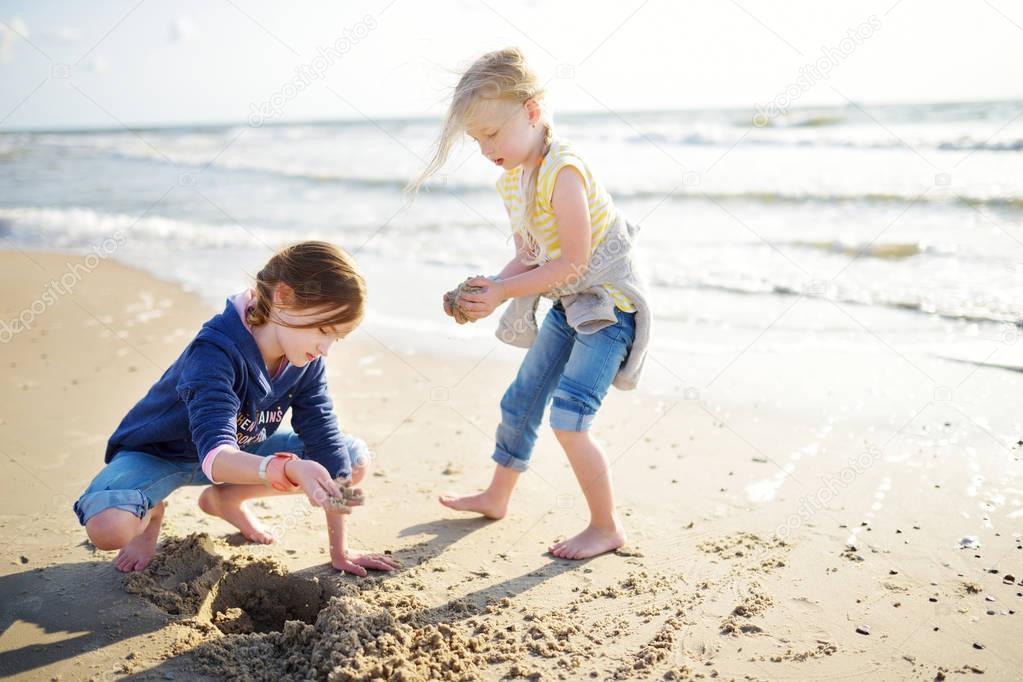 Two little sisters having fun on sandy beach by ocean.