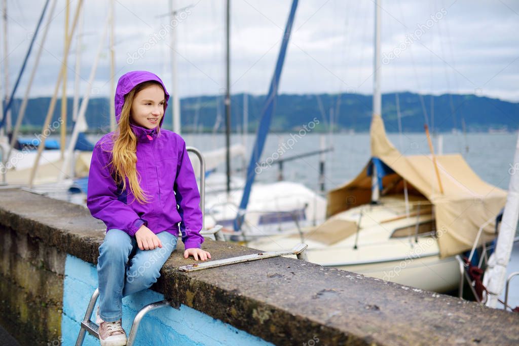 happy little girl sitting admiring yachts in harbor 