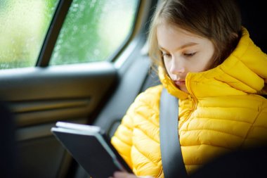Bir arabada oturan ve yağmurlu sonbahar gününde onu ebook okumak çok güzel kız. Herserf bir yolculuğa eğlenceli çocuk. Çocuklarla arabayla seyahat.