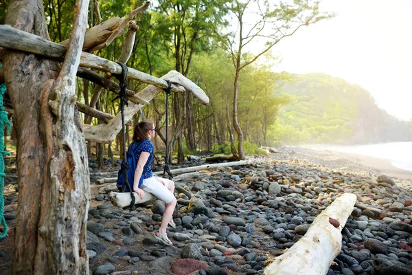 在美国夏威夷大岛 Pololu 山谷的岩石海滩上 在手工秋千上放松的年轻女子 — 图库照片