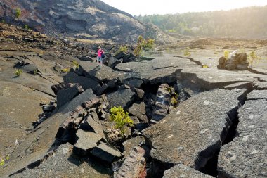 Young woman exploring surface of Kilauea Iki volcano crater with crumbling lava rock in Big Island of Hawaii, USA clipart