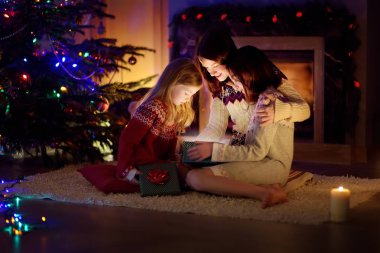 Mutlu genç anne ve iki küçük kızı Noel arifesinde karanlık bir oturma odasında şöminenin yanında sihirli bir Noel hediyesi açıyorlar..
