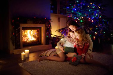 Mutlu genç anne ve iki küçük kızı Noel arifesinde karanlık bir oturma odasında şöminenin yanında sihirli bir Noel hediyesi açıyorlar..