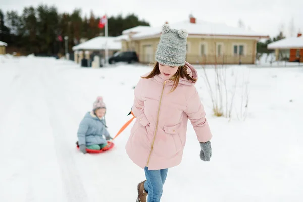 Dwie zabawne dziewczynki bawiące się saniami w pięknym zimowym parku. Cute dzieci bawiące się w śniegu. — Zdjęcie stockowe