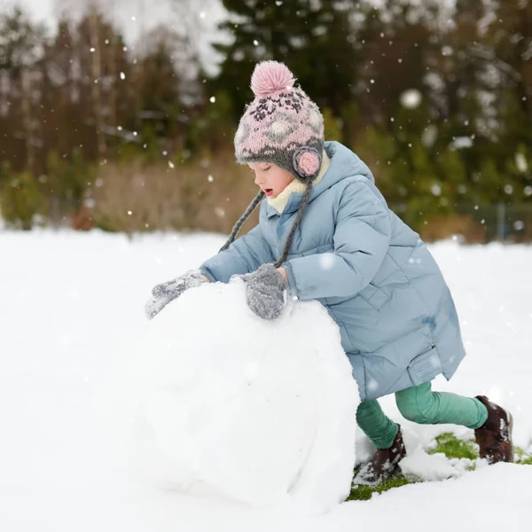 En söt ung flicka som bygger en snögubbe på bakgården. Söta barn leker i en snö. — Stockfoto