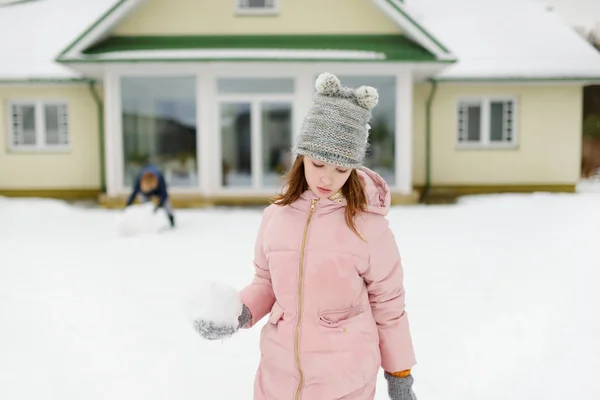 Αξιολάτρευτο κορίτσι που φτιάχνει χιονάνθρωπο στην πίσω αυλή. Χαριτωμένο παιδί που παίζει στο χιόνι. — Φωτογραφία Αρχείου