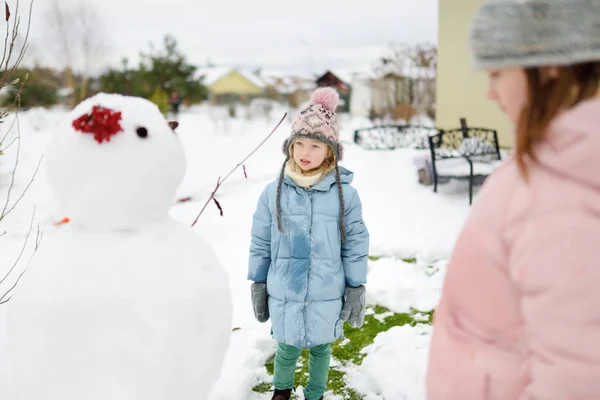 Adorables chicas jóvenes construyendo un muñeco de nieve en el patio trasero. Lindos niños jugando en la nieve. Actividades de invierno para niños . — Foto de Stock