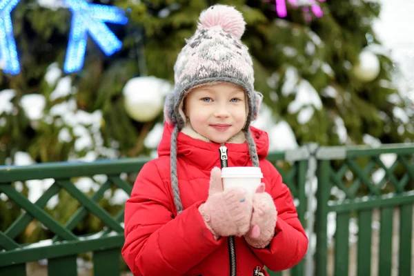Menina bonito beber chocolate quente na feira de Natal tradicional em Riga, Letónia. Criança desfrutando de doces, doces e pão de gengibre no mercado de Natal . — Fotografia de Stock