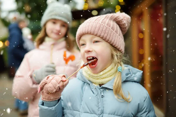 Deux adorables sœurs qui ont des sucettes en forme de coq lors de la foire traditionnelle de Noël à Riga, en Lettonie. Enfants dégustant des bonbons, des bonbons et du pain d'épice sur le marché de Noël . — Photo