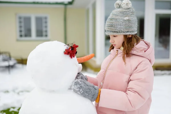 Urocza młoda dziewczyna budująca bałwana na podwórku. Cute dziecko gra w śniegu. — Zdjęcie stockowe