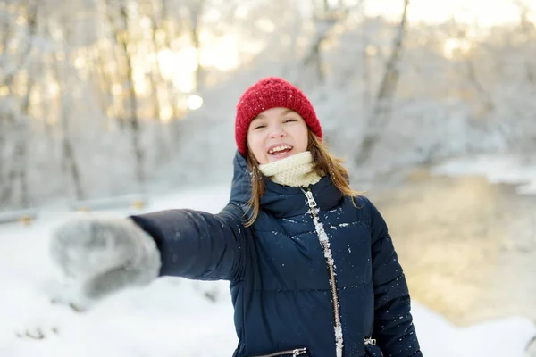 Imádnivaló fiatal lány, aki jól érzi magát a gyönyörű téli parkban. Aranyos gyerek játszik a hóban. Téli tevékenységek gyermekes családoknak. — Stock Fotó