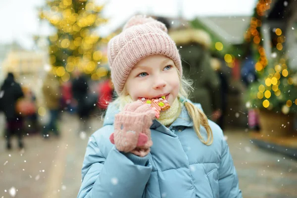 Carino giovane ragazza avendo biscotti di pan di zenzero sulla tradizionale fiera di Natale a Riga, Lettonia. Bambino godendo dolci, caramelle e pan di zenzero sul mercato di Natale . — Foto Stock