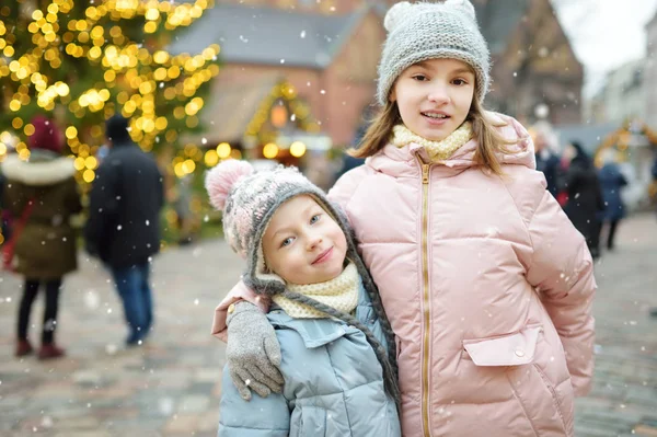 在拉脱维亚里加举行的传统圣诞博览会上，两个可爱的姐妹在一起玩得很开心。 孩子们在圣诞市场上享用糖果、糖果和姜饼. — 图库照片