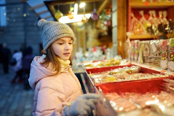Jolie jeune fille choisissant des bonbons sur le marché traditionnel de Noël à Riga, Lettonie. Enfant achetant des bonbons et des biscuits à Noël . — Photo