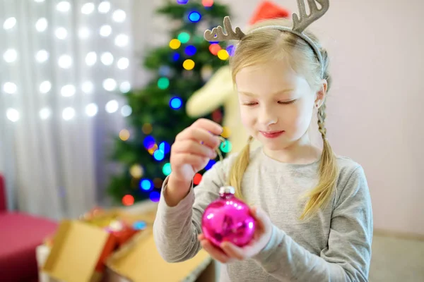 カラフルなガラスの泡でクリスマスツリーを飾る愛らしい少女。クリスマスツリーのトリミング. — ストック写真