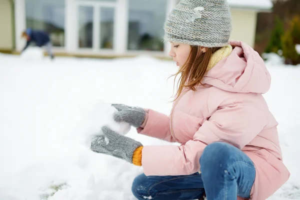 En söt ung flicka som bygger en snögubbe på bakgården. Söta barn leker i en snö. — Stockfoto