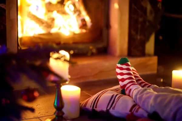 Mulher descansando as pernas em meias festivas listradas em um quarto com uma lareira acesa e velas na noite de Natal aconchegante . — Fotografia de Stock