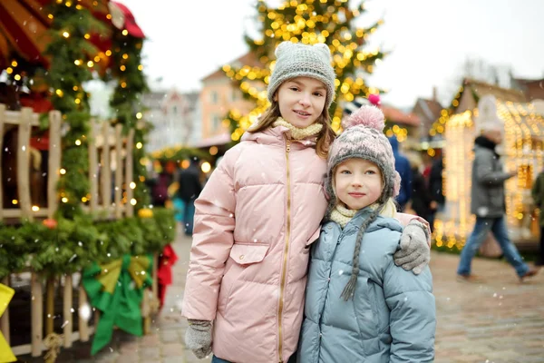 ラトビアのリガで開催される伝統的なクリスマス・フェアで楽しい時間を過ごす2人の愛らしい姉妹。クリスマスマーケットでお菓子やキャンディー、ジンジャーブレッドを楽しむ子供たち. — ストック写真