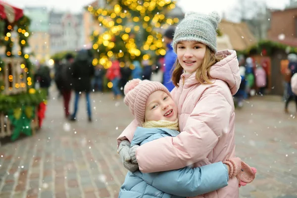 ラトビアのリガで開催される伝統的なクリスマス・フェアで楽しい時間を過ごす2人の愛らしい姉妹。クリスマスマーケットでお菓子やキャンディー、ジンジャーブレッドを楽しむ子供たち. — ストック写真
