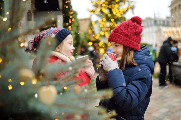 Dua suster menggemaskan minum cokelat panas pada festival Natal tradisional di Riga, Latvia. Anak-anak menikmati manisan, permen dan roti jahe di pasar Xmas . — Stok Foto