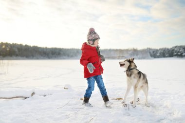 Donmuş gölün kıyısında eğlenen sevimli genç kız. Karda köpekle oynayan sevimli bir çocuk..