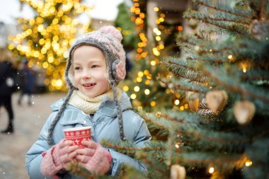 Riga, Letonya 'da geleneksel Noel festivalinde sıcak çikolata içen tatlı genç kız. Çocuk Xmas pazarında tatlı, şeker ve zencefilli ekmek yiyor.