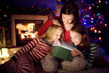 Mutlu genç anne ve iki küçük kızı Noel arifesinde karanlık bir oturma odasında şöminenin yanında sihirli bir Noel hediyesi açıyorlar..