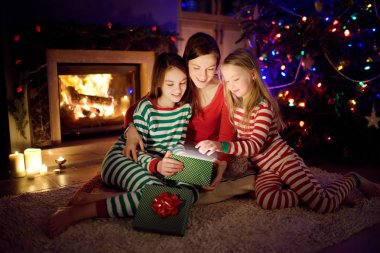 Mutlu genç anne ve iki küçük kızı Noel arifesinde karanlık bir oturma odasında şöminenin yanında sihirli bir Noel hediyesi açıyorlar..