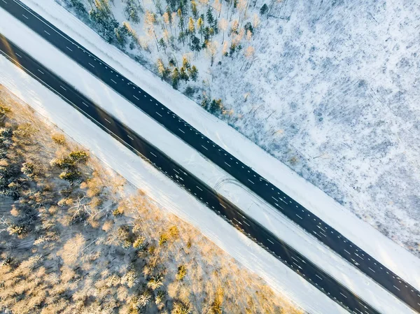 Piękny widok z lotu ptaka pokrytych śniegiem pól z dwupasmowej drogi wśród drzew. Lód rybi i szron pokrywający drzewa. — Zdjęcie stockowe