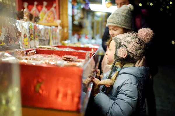 ラトビアのリガにある伝統的なクリスマスマーケットでお菓子を選ぶかわいい妹たち。クリスマスにお菓子やクッキーを買う子供たち. — ストック写真