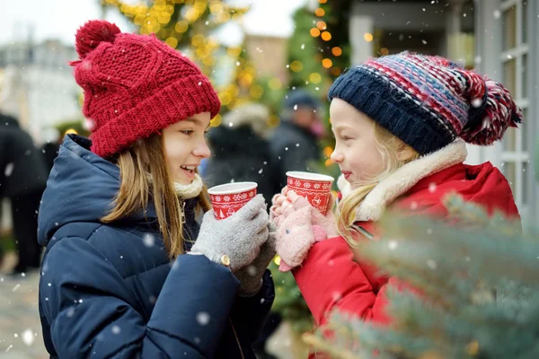 Дві прекрасні сестри п "ють гарячий шоколад на традиційному Різдвяному ярмарку в Ризі (Латвія). Діти, які люблять солодощі, цукерки та імбирні пряники на базарі Xmas.. — стокове фото
