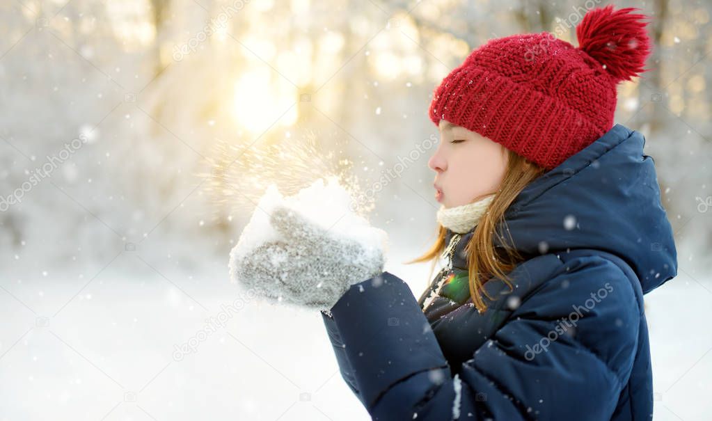 Adorable young girl having fun in beautiful winter park. Cute child playing in a snow. Winter activities for family with kids.
