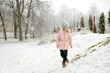 Tatlı genç kız kar yağarken güzel kış parkında eğleniyor. Karda oynayan sevimli bir çocuk. Çocuklu aileler için kış etkinlikleri.