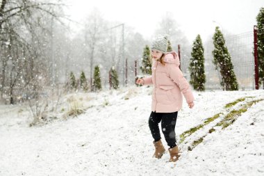 Tatlı genç kız kar yağarken güzel kış parkında eğleniyor. Karda oynayan sevimli bir çocuk. Çocuklu aileler için kış etkinlikleri.