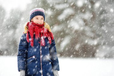 Tatlı genç kız kar yağarken güzel kış parkında eğleniyor. Karda oynayan sevimli bir çocuk. Çocuklu aileler için kış etkinlikleri.