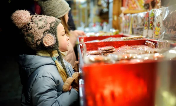 ラトビアのリガにある伝統的なクリスマスマーケットでお菓子を選ぶかわいい妹たち クリスマスにキャンディーとクッキーを買う子供たち 寒い冬の日の幸せな家族の時間 — ストック写真