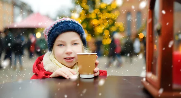 ラトビアのリガで開催される伝統的なクリスマスフェアでホットチョコレートを飲むかわいい女の子 クリスマスマーケットでお菓子やキャンディー ジンジャーブレッドを楽しむ子供たち 家族や子供と冬の時間 — ストック写真