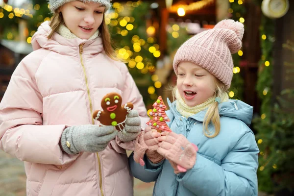 ラトビアのリガで伝統的なクリスマスフェアでジンジャーブレッドクッキーを持っている2人の愛らしい姉妹 クリスマスマーケットでお菓子やキャンディー ロリポップを楽しむ子供たち 家族や子供と冬の時間 — ストック写真