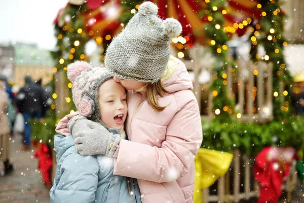 ラトビアのリガで開催される伝統的なクリスマス フェアで楽しい時間を過ごす2人の愛らしい姉妹 クリスマスマーケットでお菓子やキャンディー ジンジャーブレッドを楽しむ子供たち 家族や子供と冬の時間 — ストック写真