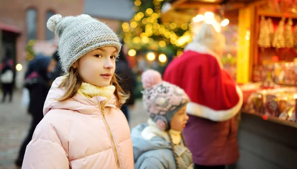 ラトビアのリガにある伝統的なクリスマスマーケットでお菓子を選ぶかわいい女の子。Xmasでキャンディとクッキーを買う子供. — ストック写真