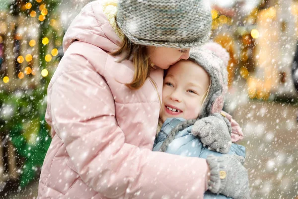 Twee schattige zusjes die zich vermaken op de traditionele kerstmarkt in Riga, Letland. Kinderen die genieten van snoep, snoep en peperkoek op de kerstmarkt. — Stockfoto