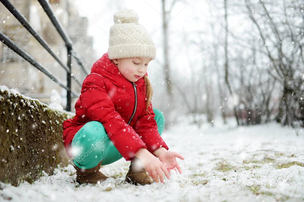 Adorable young girl having fun in beautiful winter park during snowfall. Cute child playing in a snow. Winter activities for family with kids.