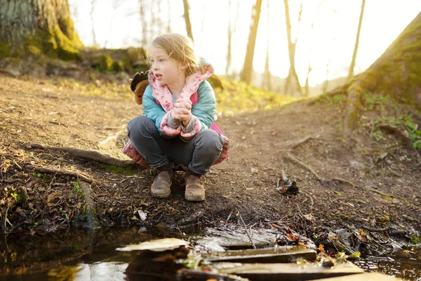 Cute młoda dziewczyna zabawy nad rzeką w ciepły wiosenny dzień. Dziecko bawiące się nad wodą. — Zdjęcie stockowe