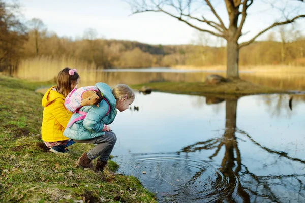 Dvě roztomilé mladé sestry se baví u řeky v teplý jarní den. Děti si spolu hrají u vody. — Stock fotografie