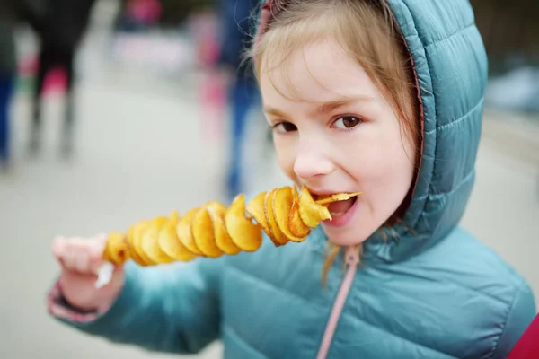 Petite fille mignonne mangeant des pommes de terre frites sur un bâton lors d'une froide journée d'hiver en plein air . — Photo